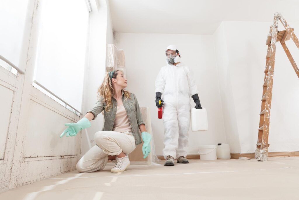 Concerned woman at a home renovation site shows a mold problem to a professional worker using products for mold remediation treatment