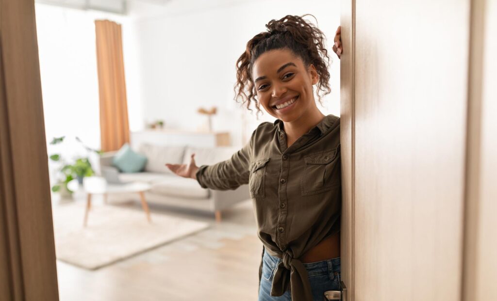 Joyful Millennial Black Lady Opening Door Welcoming Standing At Home