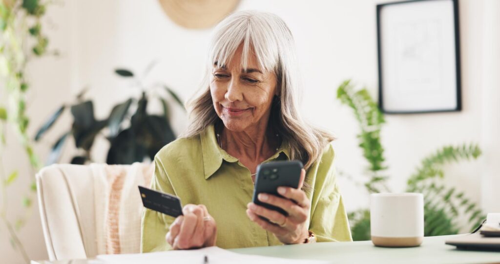 Phone, credit card and mature woman in home for online shopping or ecommerce order with sale. Relax, cellphone and female person with banking app for payment, transaction or deposit in house.