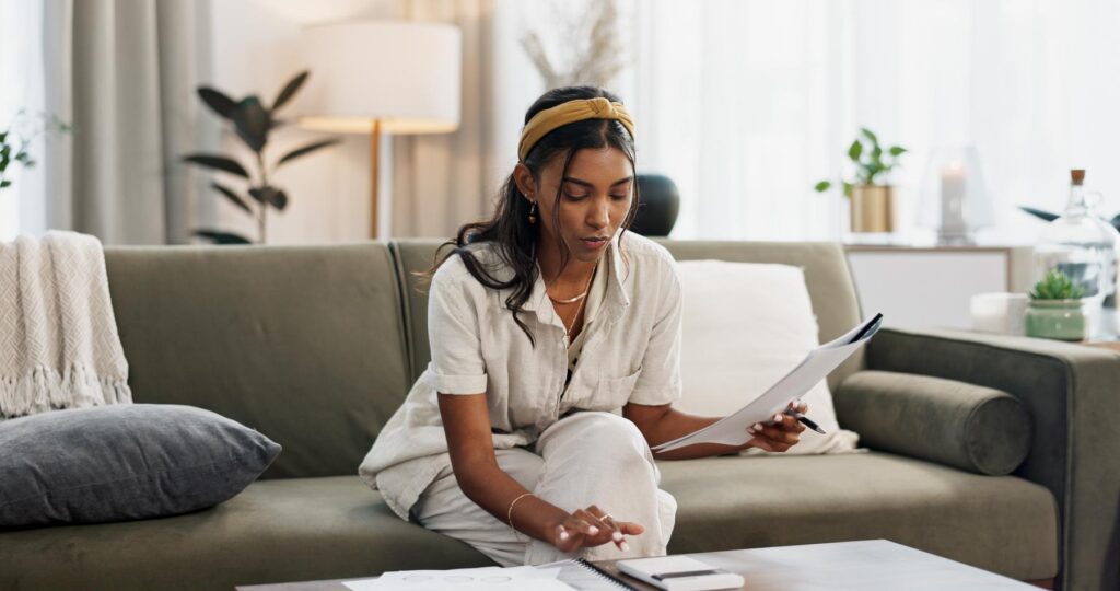 Woman, calculator and budget on sofa of home finance, taxes documents and income or salary management. Young person with paperwork, invoice or loan, inflation and bills for rent cost in living room