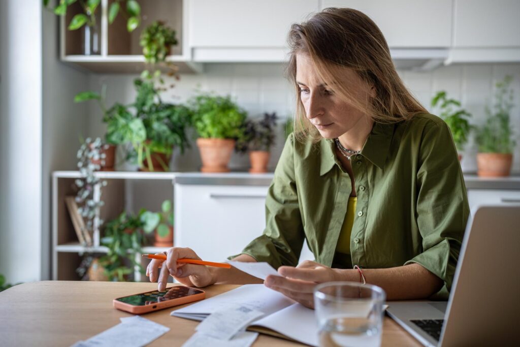 Concentrated female holding bill for utilities payment, checking figures on mobile phone calculator