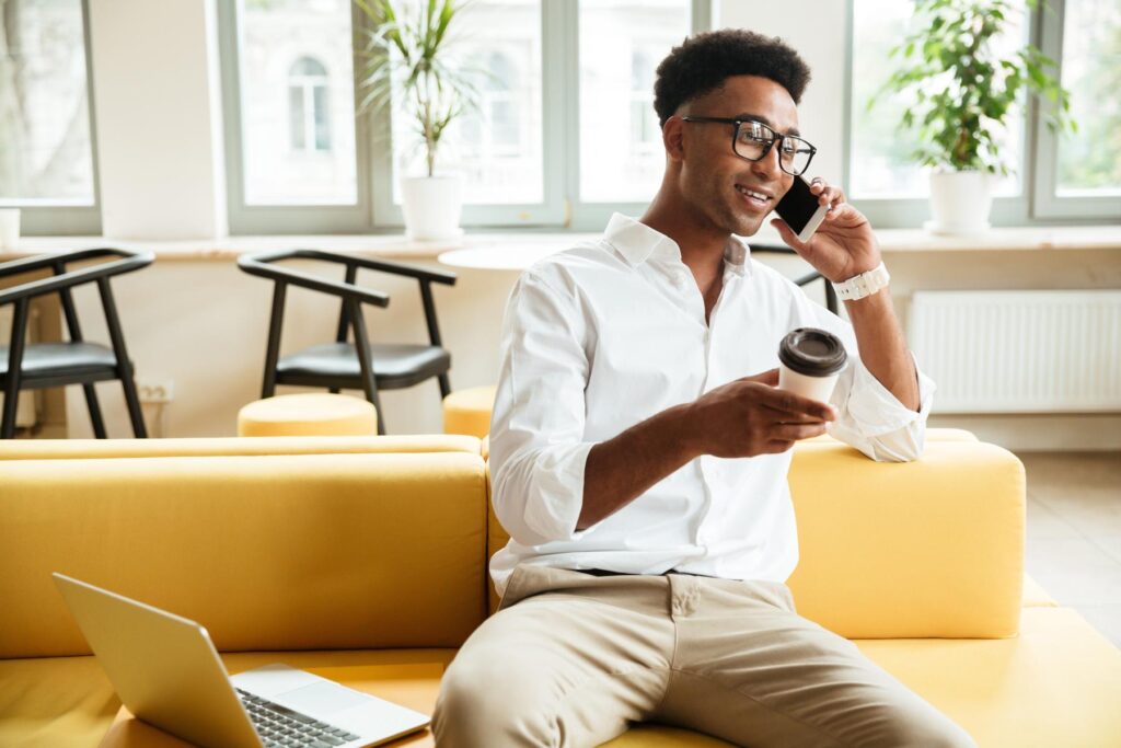 Handsome young african man talking by phone drinking coffee.