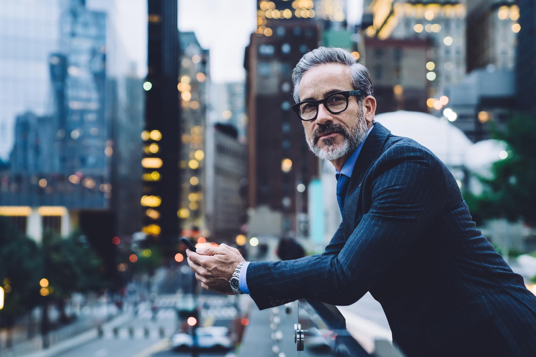 Mature businessman holding phone against background of city street