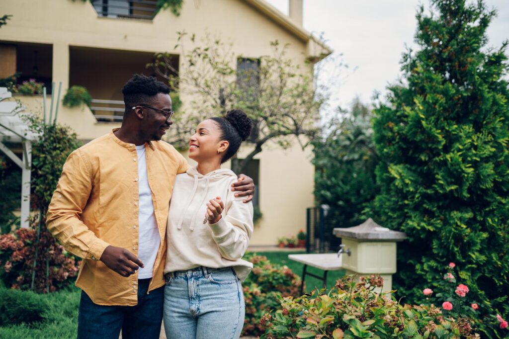 Multiracial couple holding keys and standing outside their new h