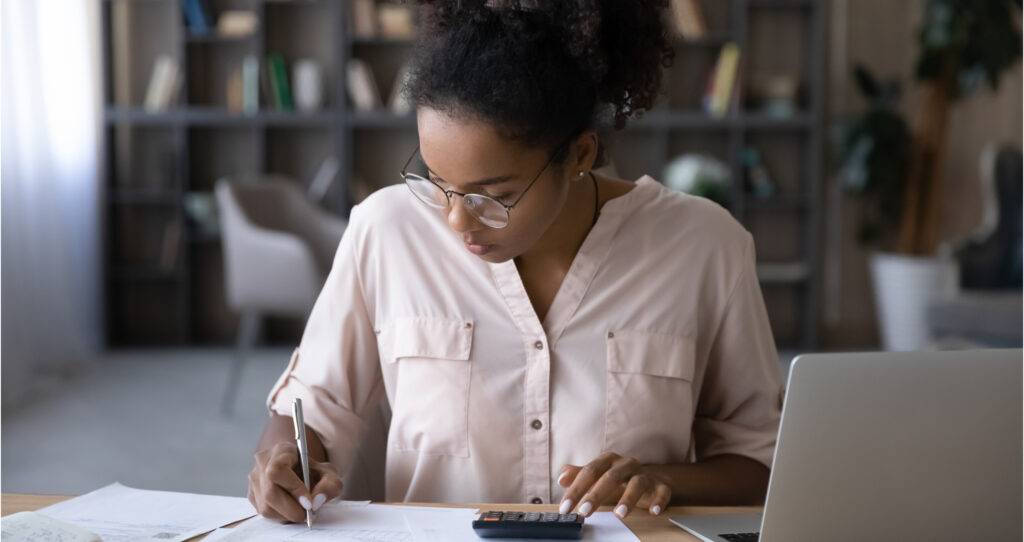woman at a desk with a laptop, paper, and calculator managing rental properties