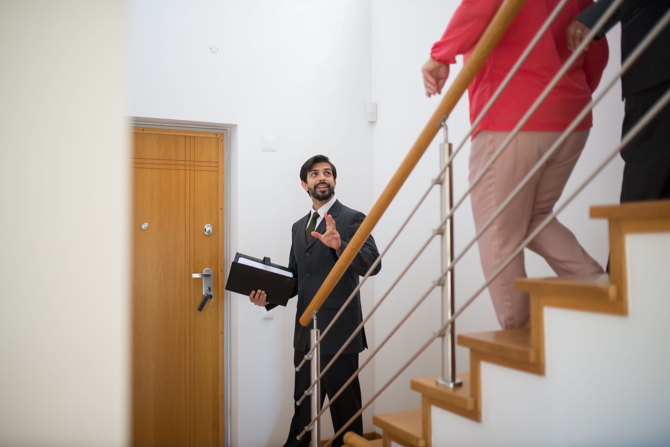 A property manager conducting a house tour with potential clients on the stairs of a modern home.