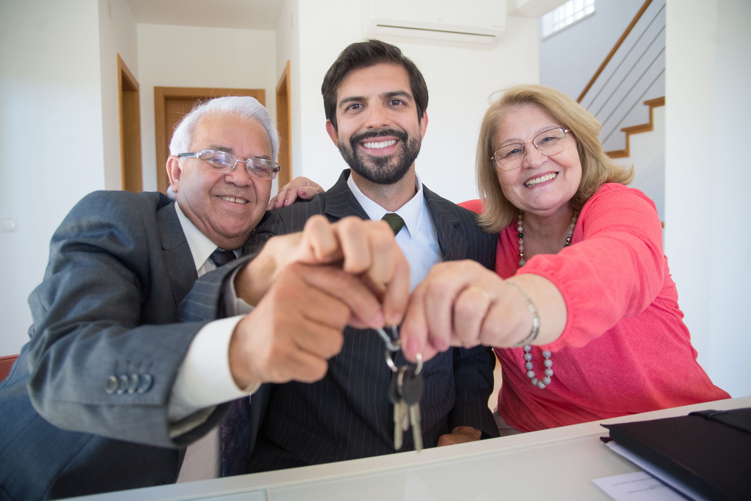 Smiling elderly couple holding house keys along with their property manager indoors.