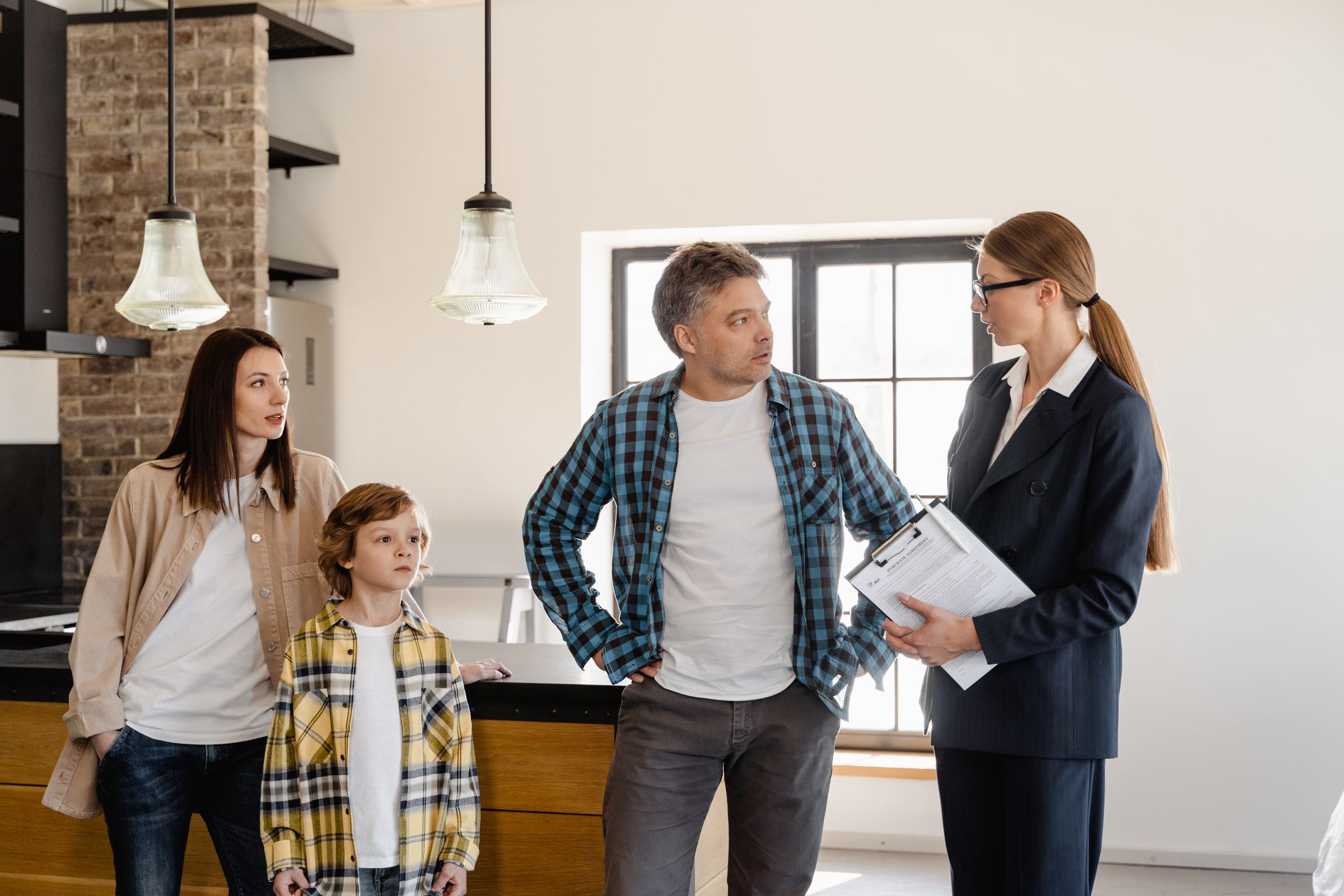 Family with child talks to a property manager in modern kitchen during home showing.