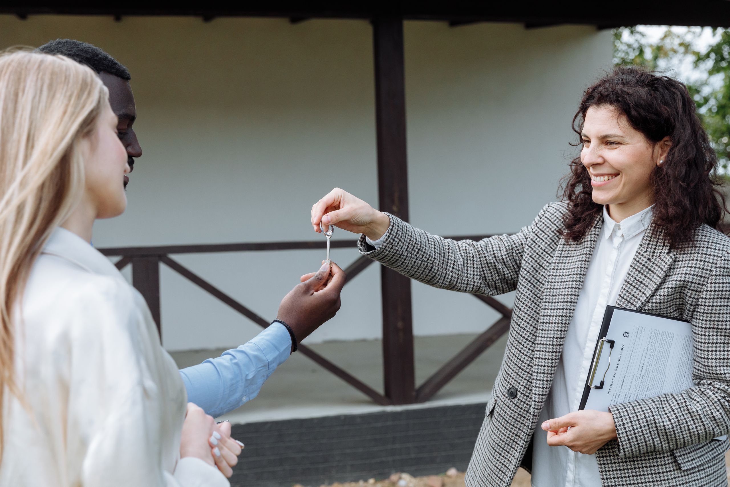 Licensed property manager giving house keys to a happy couple outside their new home.