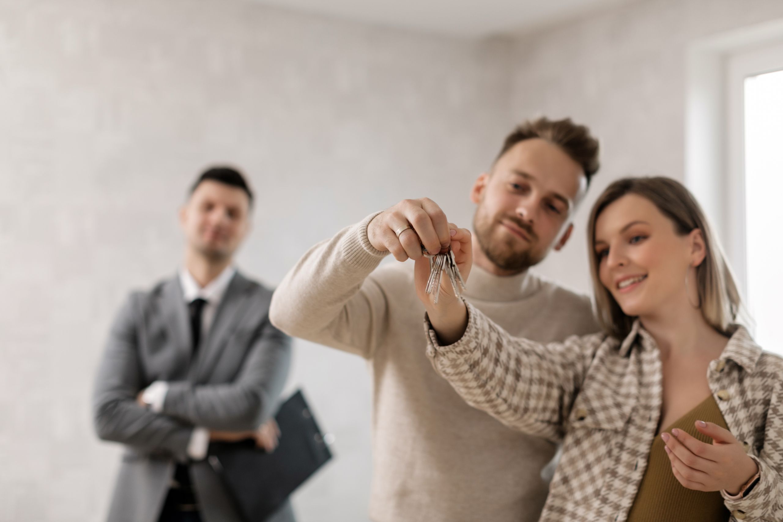 A joyful couple holding keys to their new home with a property manager in the background.