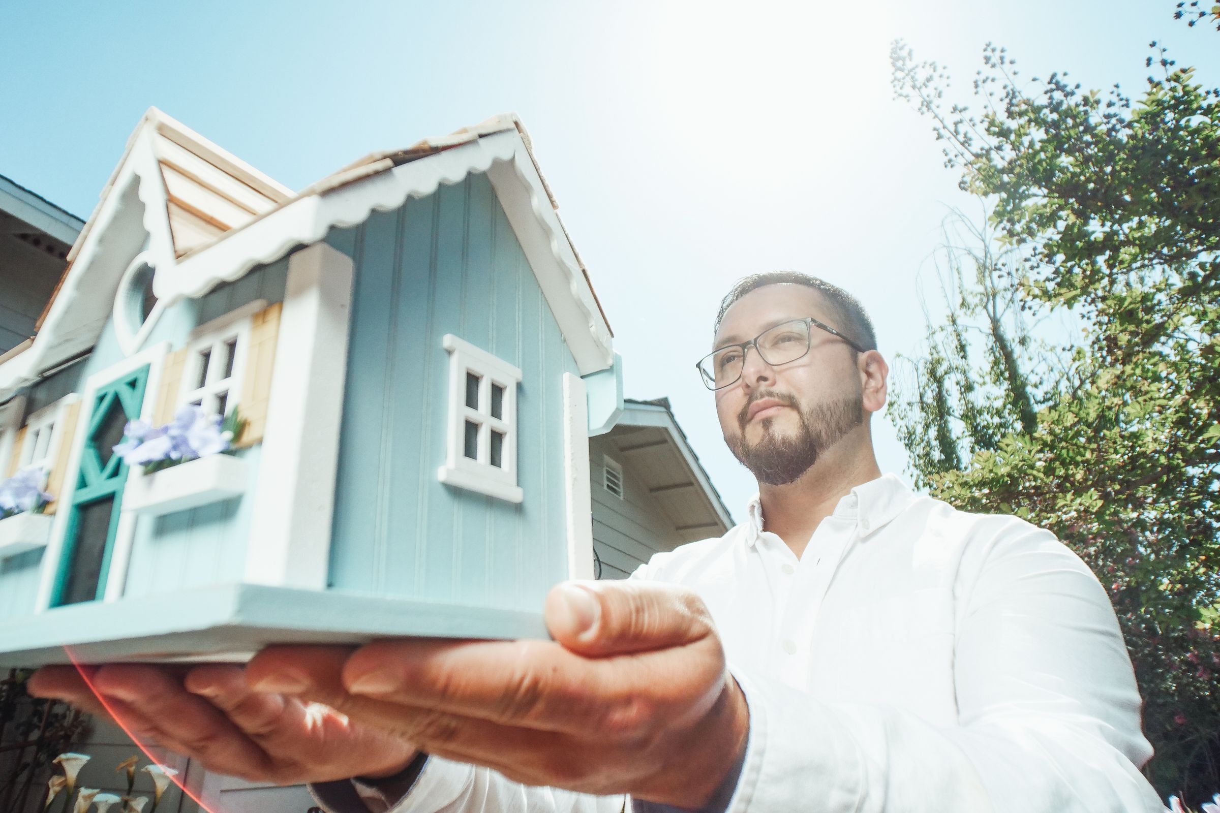 A man holds a miniature house model outdoors on a sunny day, symbolizing property management.