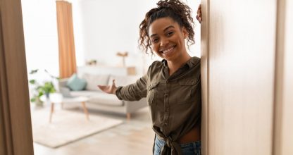 Joyful Millennial Black Lady Opening Door Welcoming Standing At Home