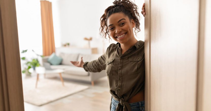 Joyful Millennial Black Lady Opening Door Welcoming Standing At Home