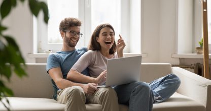 Overjoyed young couple in love cuddle on sofa using notebook