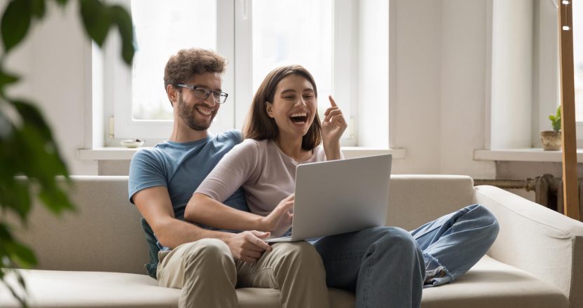 Overjoyed young couple in love cuddle on sofa using notebook