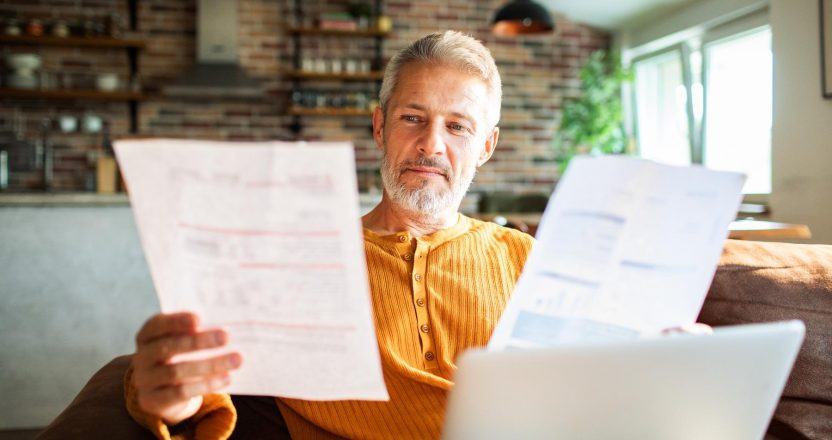Mature man reviewing bills with laptop at home, focused