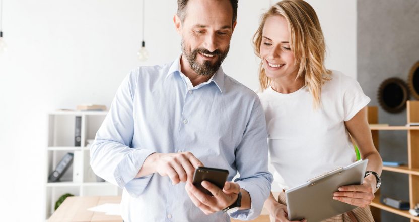 Couple of smiling colleagues looking at mobile phone