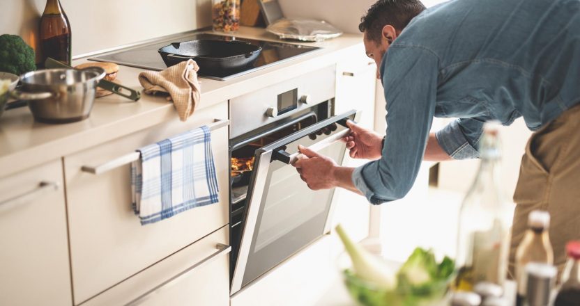 Young man cooking meat in oven at home