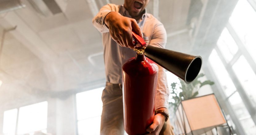 handsome businessman holding extinguisher and yelling in office with smoke
