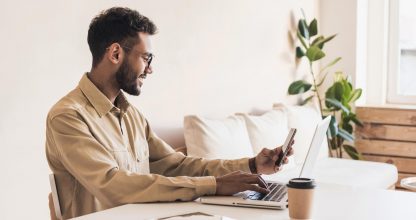 Young handsome man using smart phone and laptop at home. Businessman or student working on computer and texting smartphone. Freelance, education and technology concept