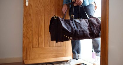 Midsection of young man with bag entering front door when coming back home.