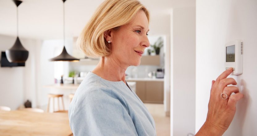 Close Up Of Mature Woman Adjusting Central Heating Temperature At Home On Thermostat
