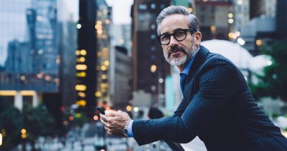 Mature businessman holding phone against background of city street