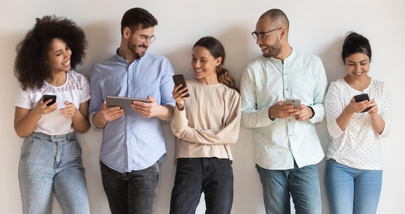 Happy diverse young people using different electronic devices.