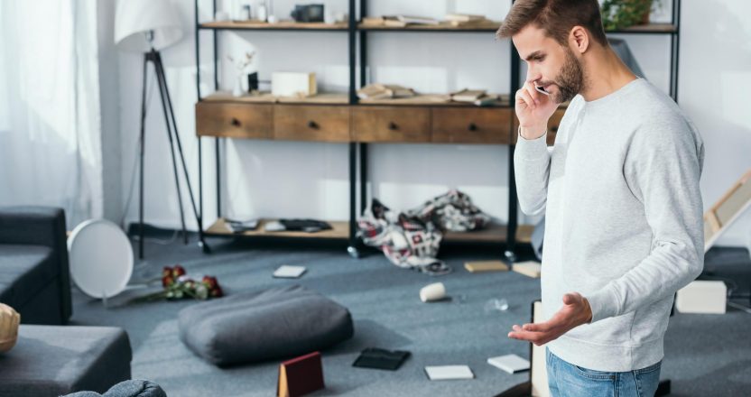 side view of handsome man talking on smartphone in robbed apartm