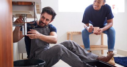 Male Plumber Teaching Female Apprentice To Fix Leaking Sink In Home Bathroom