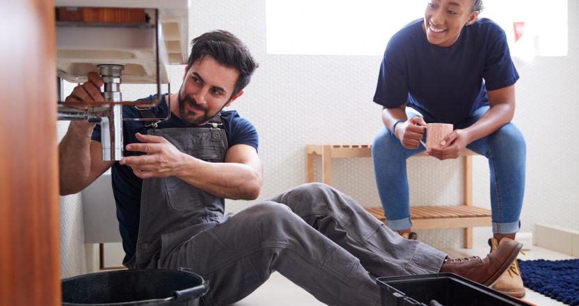 Male Plumber Teaching Female Apprentice To Fix Leaking Sink In Home Bathroom