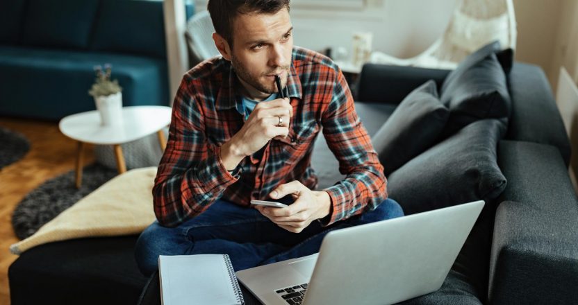 Young pensive man working at home and thinking of something.