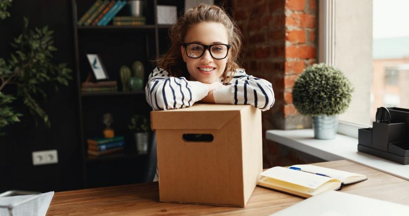 Happy woman with carton box at table in loft office