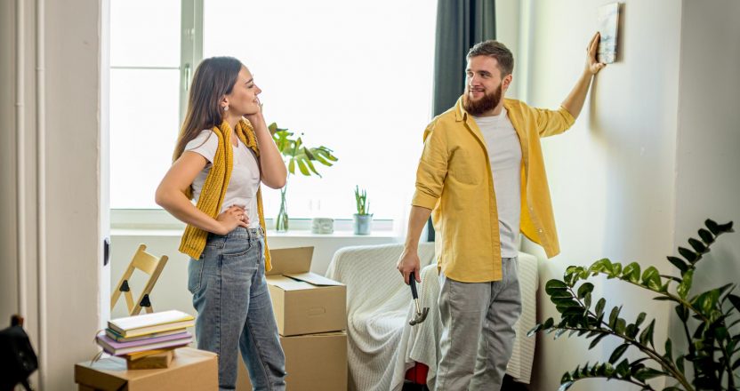 young happy couple hanging picture on the wall of living room