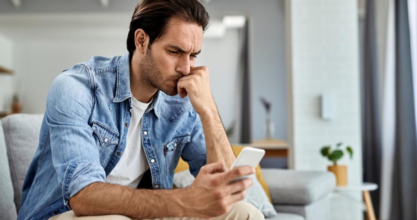 Distraught man reading text message on cell phone at home.