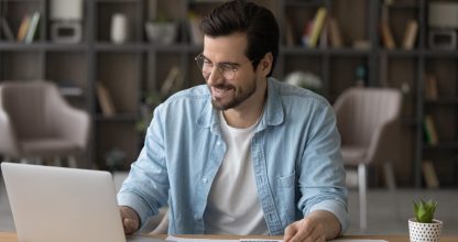 Smiling businessman in glasses using laptop, calculating bills, managing finances