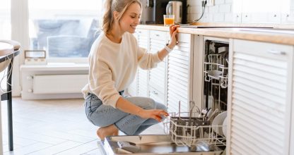 Smiling young white woman putting dishes in the dishwasher at home