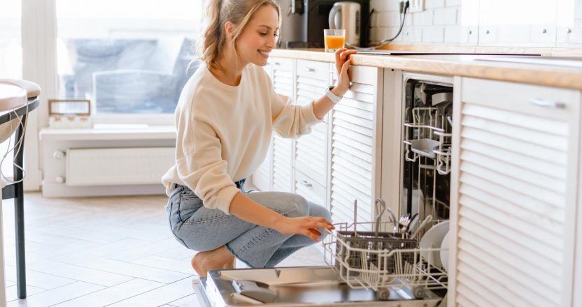 Smiling young white woman putting dishes in the dishwasher at home