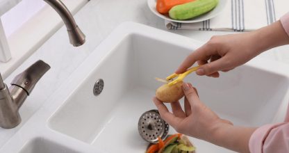 Woman peeling potato over kitchen sink with garbage disposal at