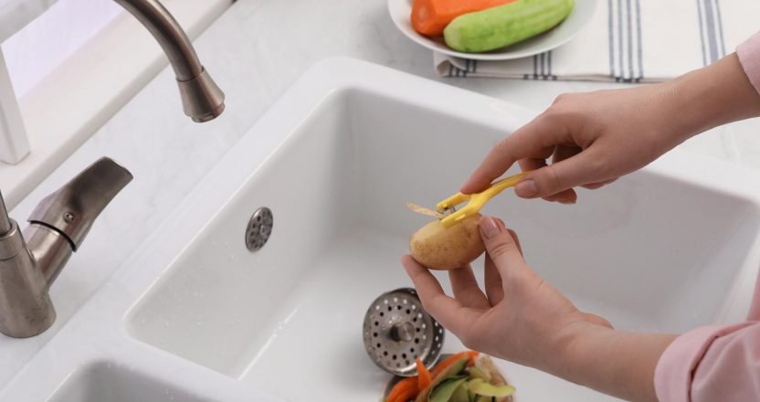 Woman peeling potato over kitchen sink with garbage disposal at