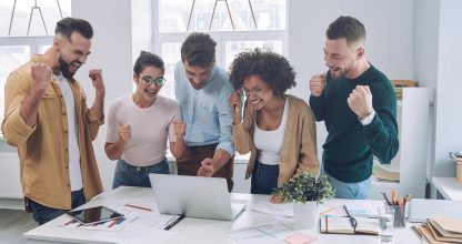 Group of happy young people in smart casual wear looking at laptop and gesturing while having meeting in the office