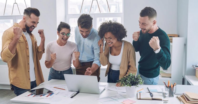 Group of happy young people in smart casual wear looking at laptop and gesturing while having meeting in the office