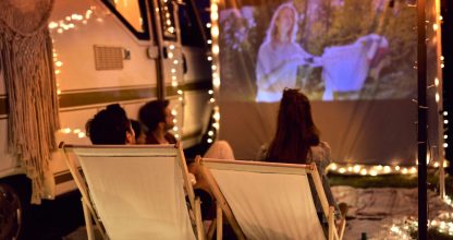 Young cheerful people watching a movie on camping site