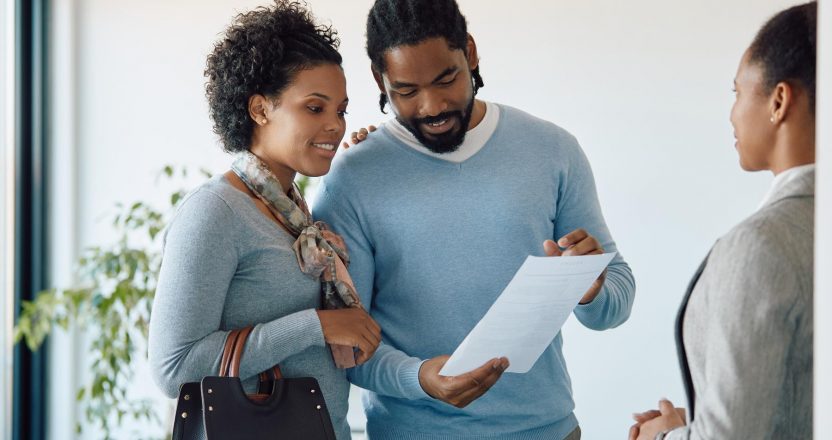 Happy black couple reading contract during meeting with insurance agent in the office.