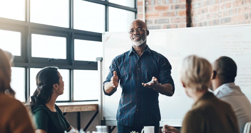 Senior business man doing presentation, planning and talking in a meeting, seminar or training workshop in a boardroom. Manager sharing ideas, teaching and coaching new employees during conference