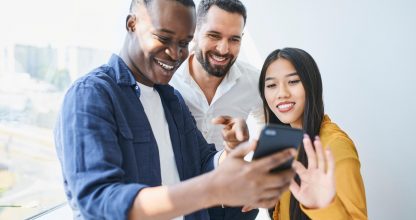 Happy coworkers looking at phone in office. Students share smartphone at university