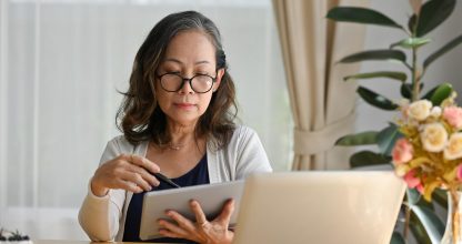 Old woman at home using laptop wearing eyeglasses working on computer.