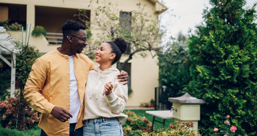 Multiracial couple holding keys and standing outside their new h