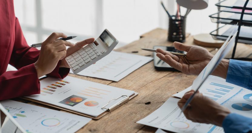 Group of businessmen, investors brainstorm to analyze financial report situation Calculate investment, income, tax with graph calculator. Growth chart with data recorded on laptop inside office.