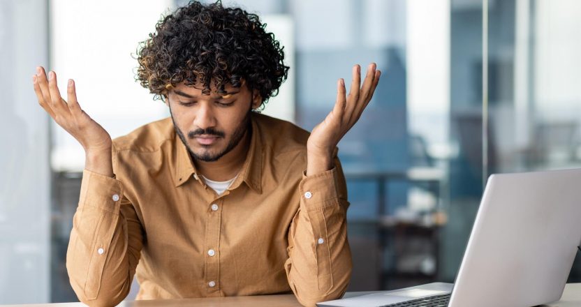 Upset financier looking at sales and revenue chart of company, businessman inside office disappointed with sales results and achievements, Hispanic man sitting at table with documents and laptop